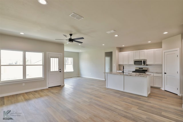 kitchen featuring ceiling fan, light wood-type flooring, gas range oven, white cabinetry, and light stone countertops