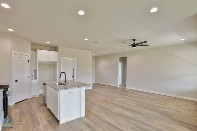 kitchen with ceiling fan, light wood-type flooring, white cabinets, light stone counters, and sink