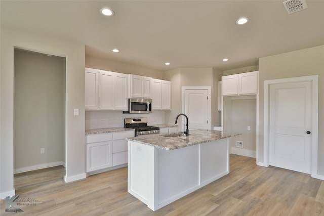 kitchen featuring white cabinets, light hardwood / wood-style flooring, a center island with sink, and stainless steel appliances