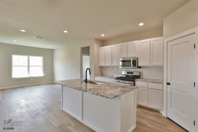 kitchen featuring appliances with stainless steel finishes, light hardwood / wood-style flooring, backsplash, white cabinetry, and sink