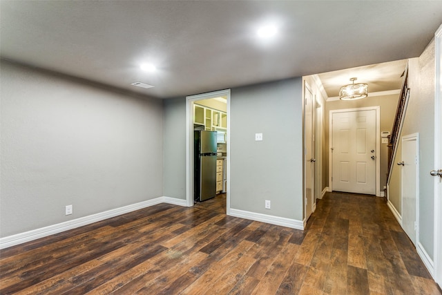 spare room featuring dark wood-style flooring, visible vents, crown molding, and baseboards