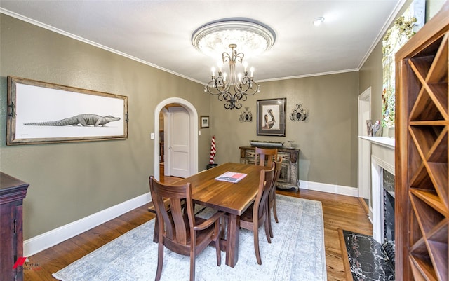 dining area with baseboards, arched walkways, wood finished floors, an inviting chandelier, and crown molding