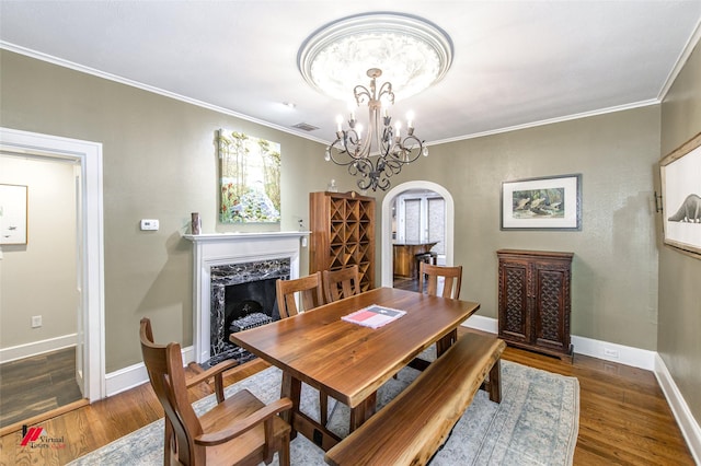 dining area with arched walkways, crown molding, a fireplace, visible vents, and wood finished floors