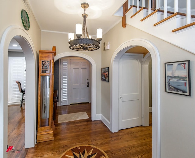 foyer entrance with baseboards, arched walkways, ornamental molding, wood finished floors, and a chandelier