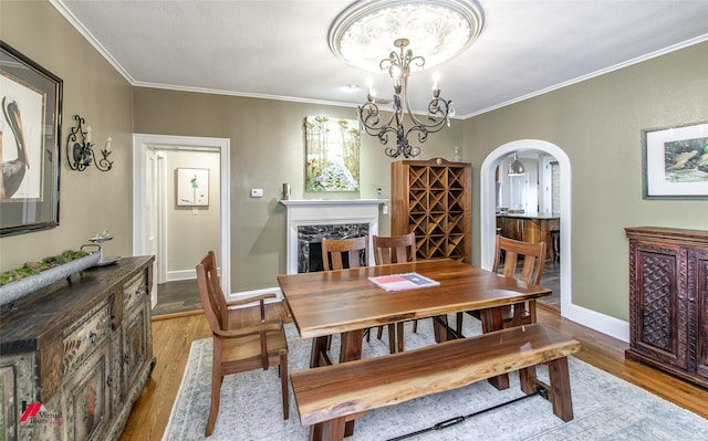 dining room with ornamental molding, arched walkways, wood finished floors, and an inviting chandelier