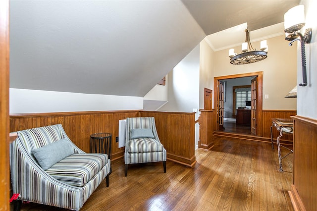 living area with lofted ceiling, hardwood / wood-style flooring, wooden walls, wainscoting, and an inviting chandelier