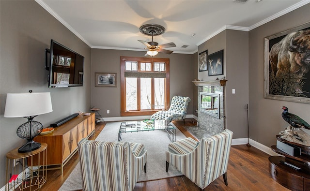 living area with baseboards, ceiling fan, ornamental molding, wood finished floors, and a fireplace