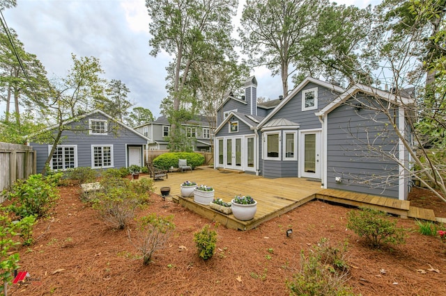 rear view of property with french doors, a chimney, fence, an outdoor structure, and a wooden deck