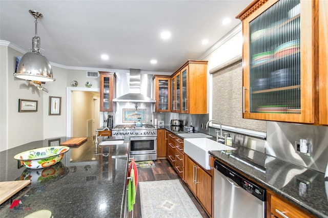 kitchen with stainless steel appliances, brown cabinetry, a sink, and wall chimney range hood