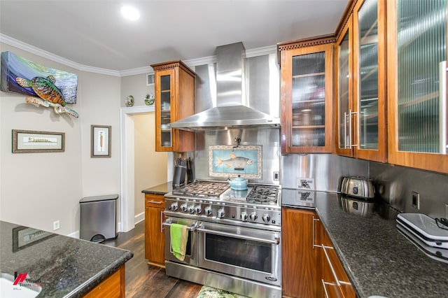 kitchen with brown cabinetry, range with two ovens, wall chimney exhaust hood, ornamental molding, and backsplash