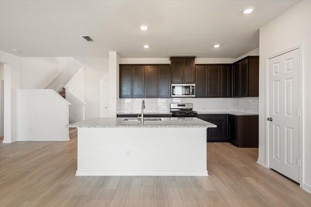 kitchen featuring appliances with stainless steel finishes, light stone counters, light hardwood / wood-style floors, sink, and tasteful backsplash