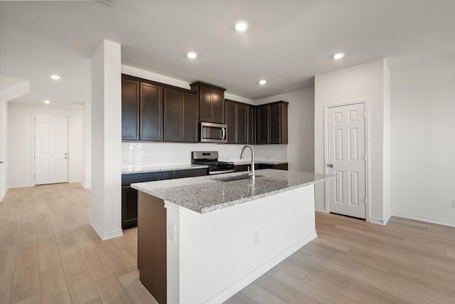 kitchen with stainless steel appliances, light wood-type flooring, and a kitchen island with sink