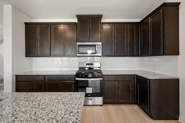 kitchen with light hardwood / wood-style floors, light stone counters, stainless steel appliances, and decorative backsplash