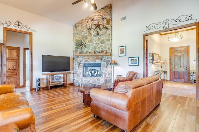 living room with hardwood / wood-style flooring, a stone fireplace, high vaulted ceiling, and ceiling fan