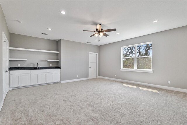 unfurnished living room with ceiling fan, light carpet, and sink