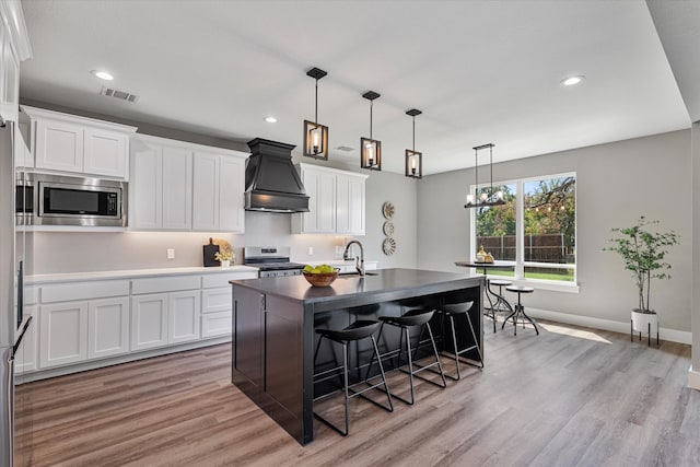 kitchen featuring light wood-type flooring, appliances with stainless steel finishes, premium range hood, and white cabinetry