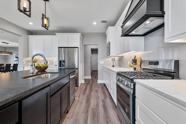 kitchen featuring light wood-type flooring, appliances with stainless steel finishes, white cabinetry, sink, and pendant lighting