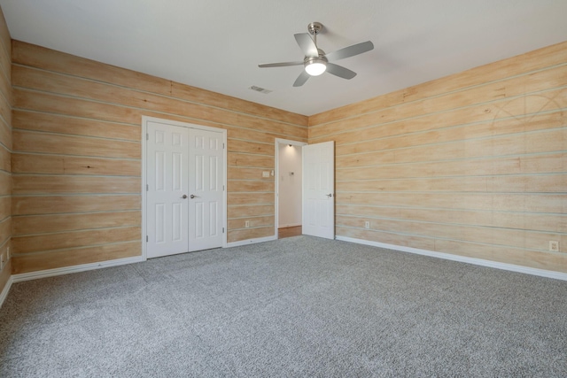 unfurnished bedroom featuring carpet flooring, a closet, ceiling fan, and wooden walls