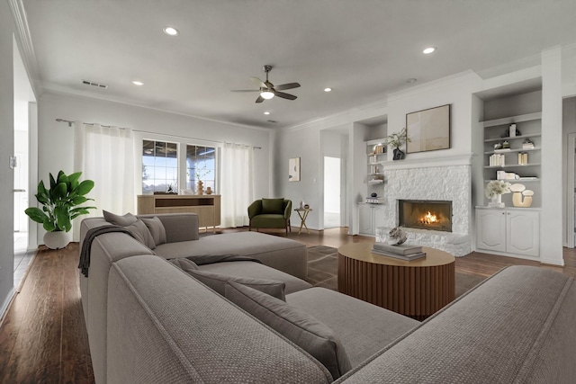 living room with built in shelves, ceiling fan, dark hardwood / wood-style flooring, a fireplace, and ornamental molding