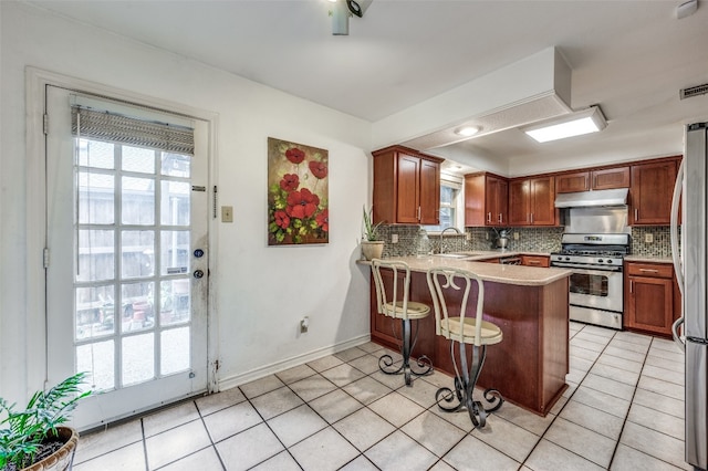 kitchen with light tile floors, appliances with stainless steel finishes, tasteful backsplash, and kitchen peninsula