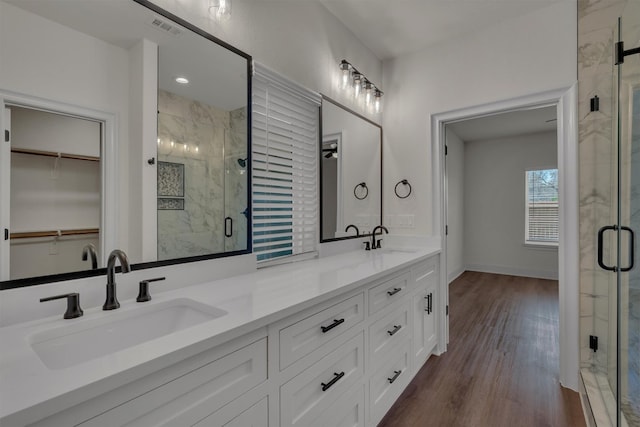 bathroom featuring a shower with shower door, double sink, oversized vanity, and wood-type flooring