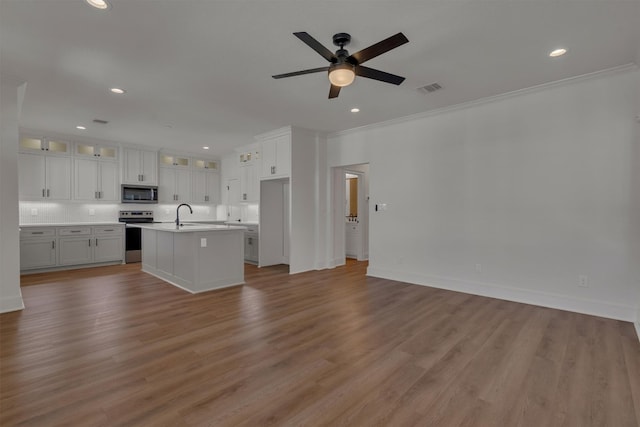 interior space featuring an island with sink, ceiling fan, white cabinets, appliances with stainless steel finishes, and light wood-type flooring