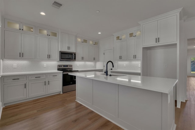 kitchen featuring appliances with stainless steel finishes, light hardwood / wood-style flooring, a center island with sink, and white cabinets