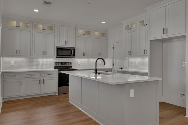 kitchen with appliances with stainless steel finishes, light hardwood / wood-style floors, white cabinetry, a center island with sink, and sink