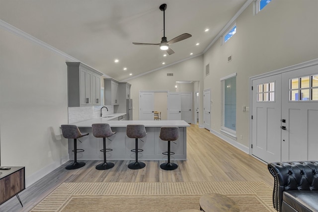 kitchen with a kitchen breakfast bar, ceiling fan, light hardwood / wood-style flooring, crown molding, and gray cabinetry