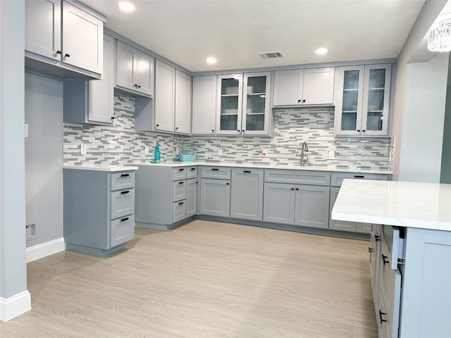 kitchen featuring light wood-type flooring, light stone counters, sink, and decorative backsplash