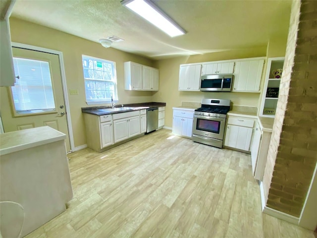 kitchen featuring brick wall, stainless steel appliances, white cabinetry, and light wood-type flooring