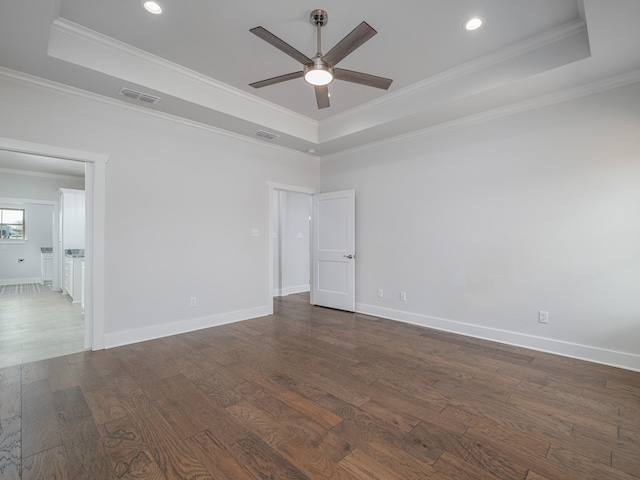 empty room featuring ornamental molding, dark wood-type flooring, ceiling fan, and a raised ceiling