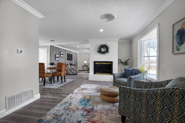 living room featuring a brick fireplace, dark wood-type flooring, ornamental molding, and a textured ceiling