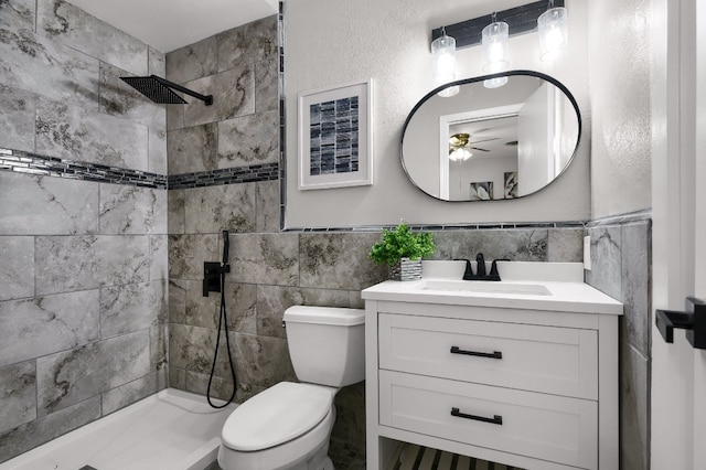 bathroom with tile walls, ceiling fan, large vanity, toilet, and a tile shower