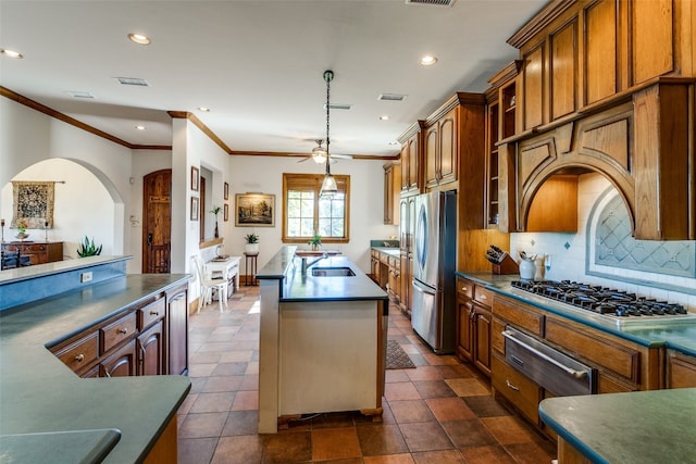 kitchen with ceiling fan, stainless steel appliances, tasteful backsplash, decorative light fixtures, and a center island with sink