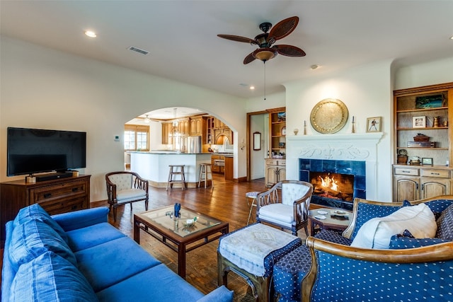 living room with a fireplace, ceiling fan, and dark wood-type flooring