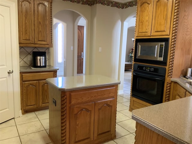 kitchen featuring tasteful backsplash, a kitchen island, light tile floors, stainless steel microwave, and oven