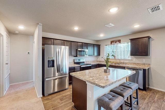 kitchen featuring dark brown cabinetry, a kitchen island, light hardwood / wood-style flooring, stainless steel appliances, and a kitchen bar