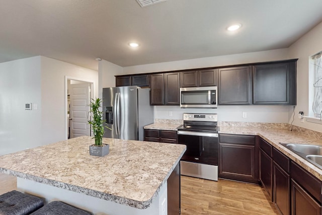 kitchen featuring appliances with stainless steel finishes, a breakfast bar, a kitchen island, light wood-type flooring, and dark brown cabinetry