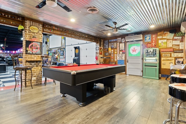 recreation room with ceiling fan, visible vents, an AC wall unit, and wood finished floors