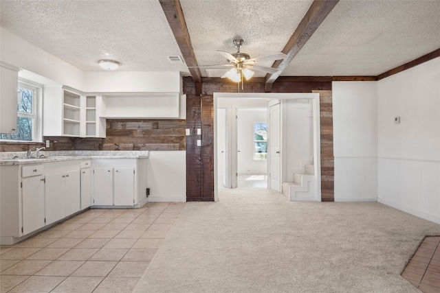 kitchen featuring white cabinets, plenty of natural light, light carpet, and beamed ceiling