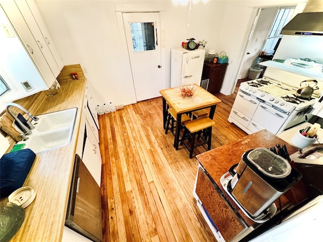 interior space featuring white gas range, light hardwood / wood-style floors, wall chimney range hood, white cabinets, and sink