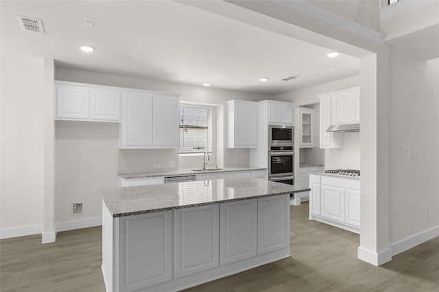 kitchen with light stone counters, appliances with stainless steel finishes, a center island, light wood-type flooring, and white cabinetry