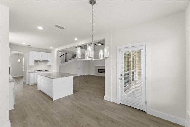 kitchen with light stone counters, white cabinets, light hardwood / wood-style floors, backsplash, and pendant lighting