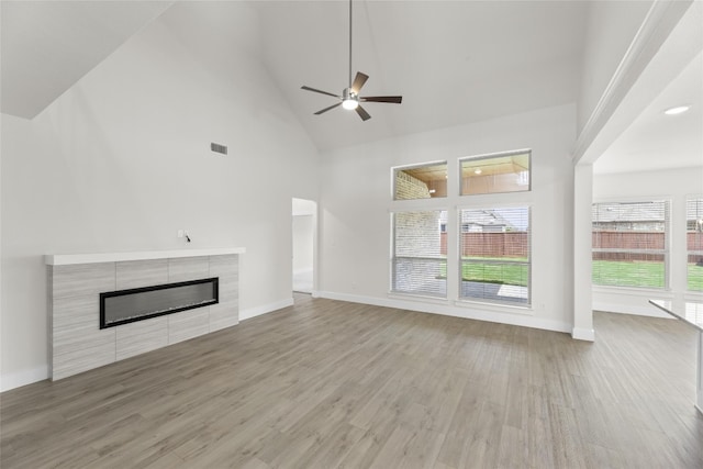 unfurnished living room with ceiling fan, a tiled fireplace, light hardwood / wood-style flooring, and high vaulted ceiling