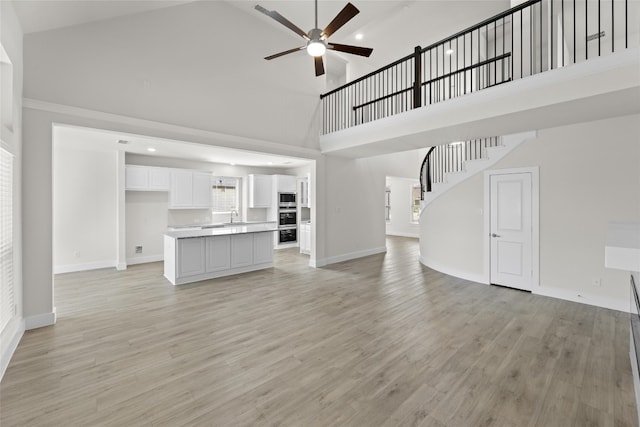 unfurnished living room with ceiling fan, high vaulted ceiling, sink, and light wood-type flooring