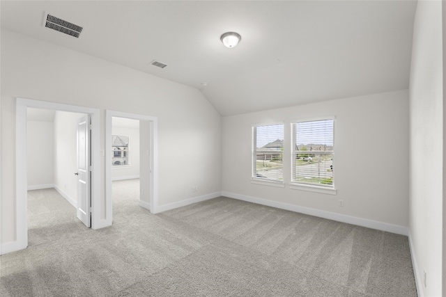 spare room featuring light colored carpet and vaulted ceiling