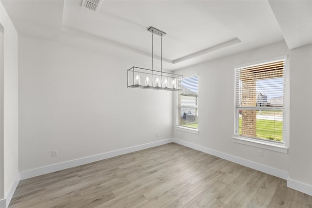 empty room with a notable chandelier, light hardwood / wood-style floors, and a raised ceiling