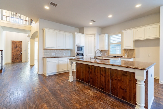 kitchen featuring backsplash, white cabinets, appliances with stainless steel finishes, and dark wood-type flooring