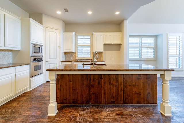 kitchen featuring dark wood-type flooring, appliances with stainless steel finishes, white cabinetry, a kitchen island with sink, and backsplash